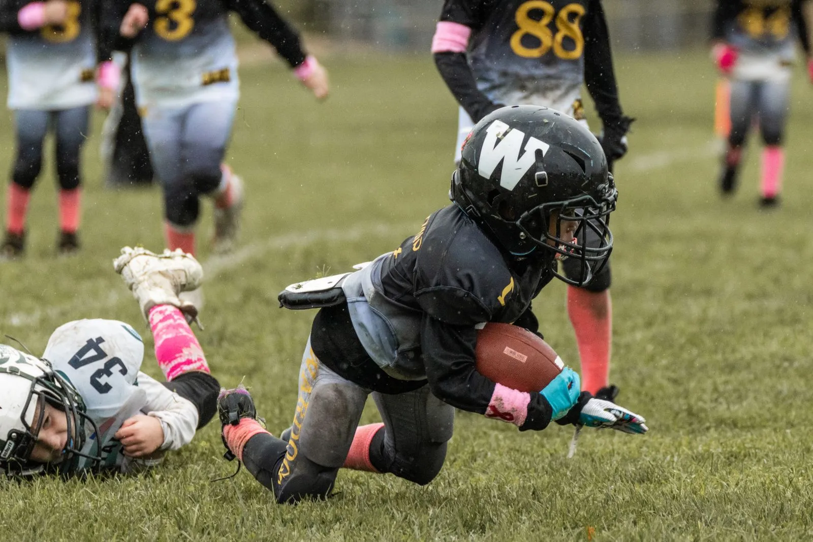 A young ball carrier diving forward with the football during a youth game
